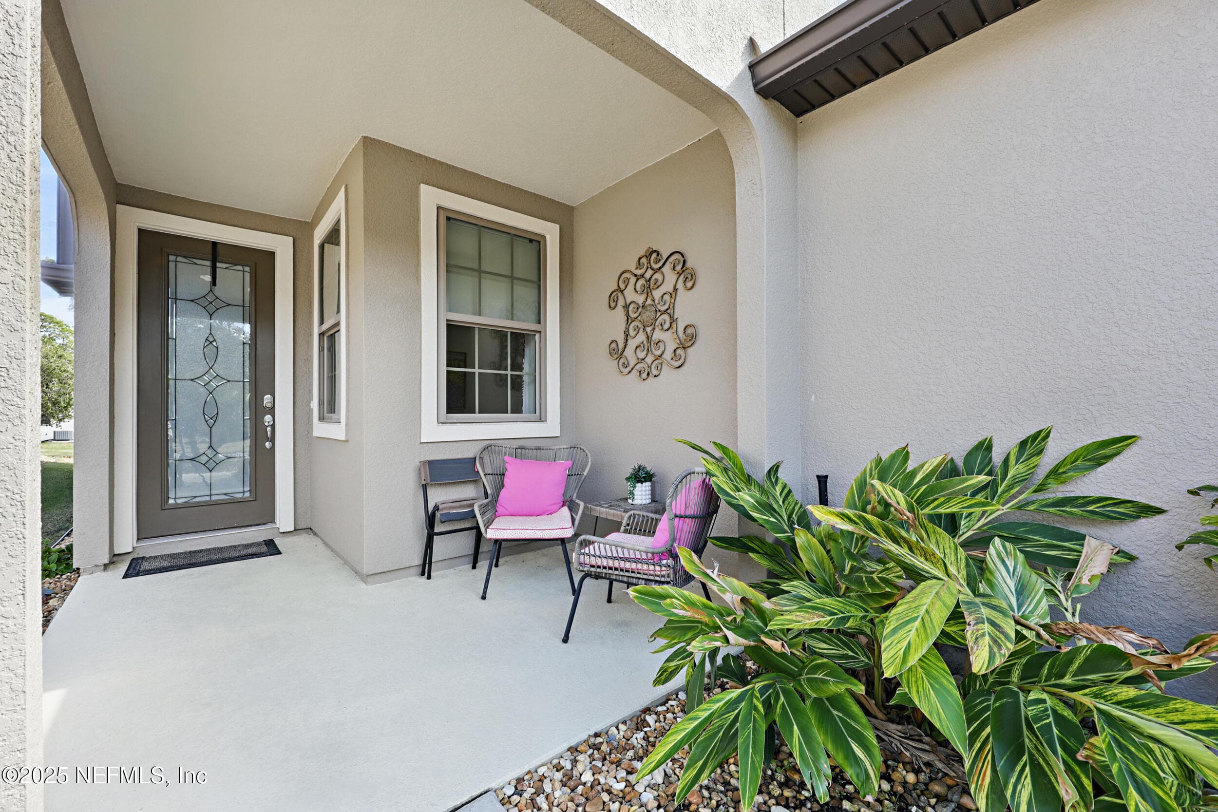 Covered front porch — Covered entry with concrete patio, decorative leaded glass front door, grid-pattern window, and river rock landscape bed with tropical plants. — 92 CANOPY OAK Lane, Ponte Vedra, FL 32081