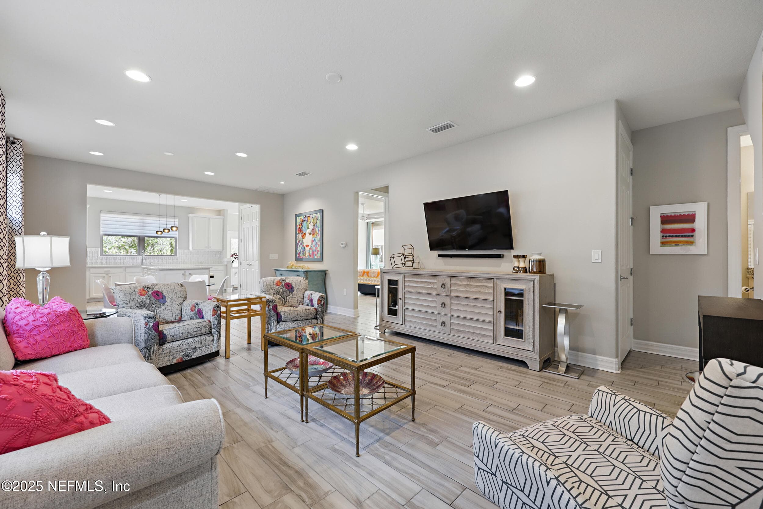 Living room — Open-concept living room with wood-look tile flooring, recessed lighting, wall-mounted TV area, and sightline through to the kitchen with white cabinetry. Neutral gray walls throughout. — 92 CANOPY OAK Lane, Ponte Vedra, FL 32081