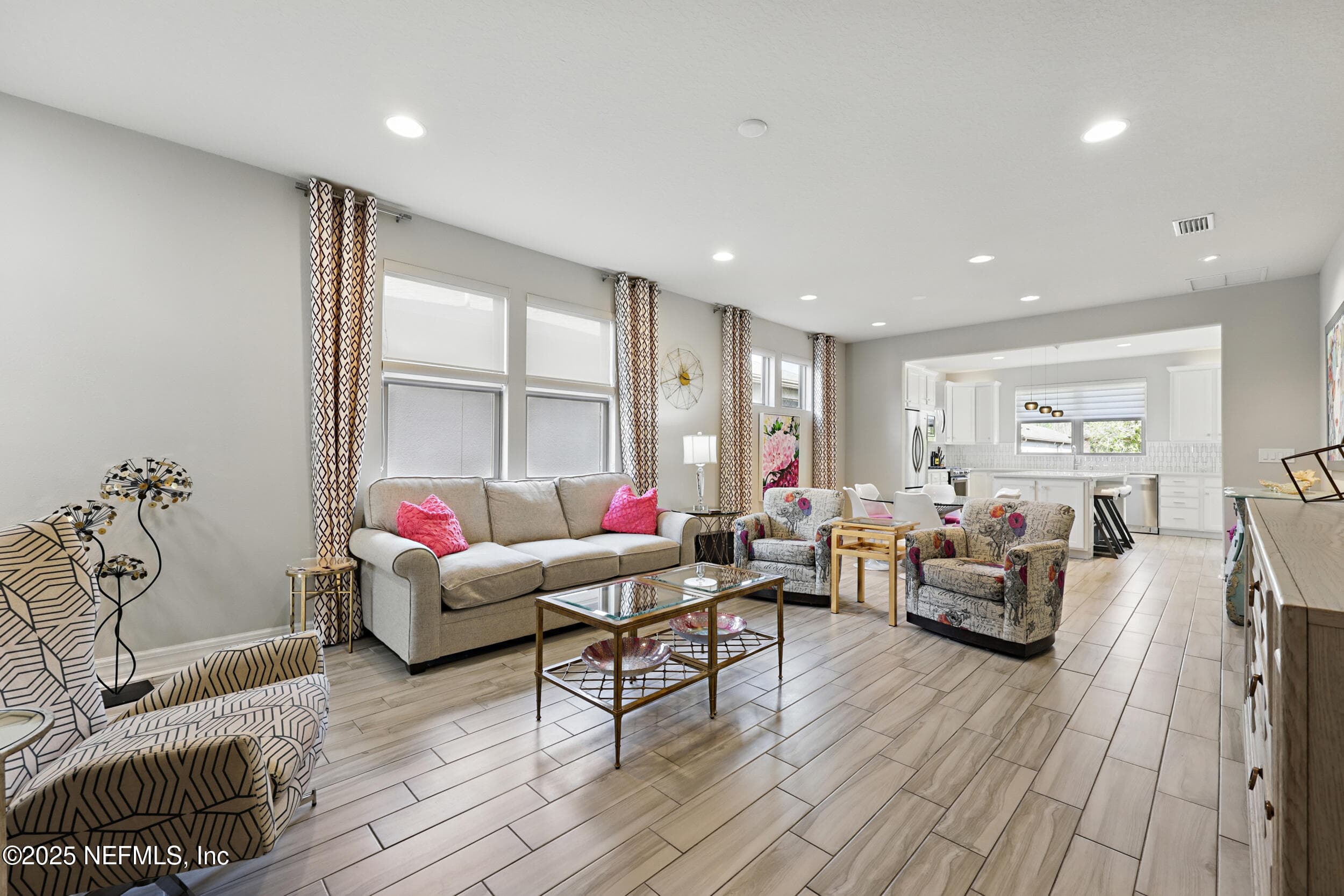 Living room (window wall) — Spacious living area with three large windows for natural light, wood-look tile flooring, recessed lighting, and open flow into the kitchen with white cabinets and tile backsplash. — 92 CANOPY OAK Lane, Ponte Vedra, FL 32081