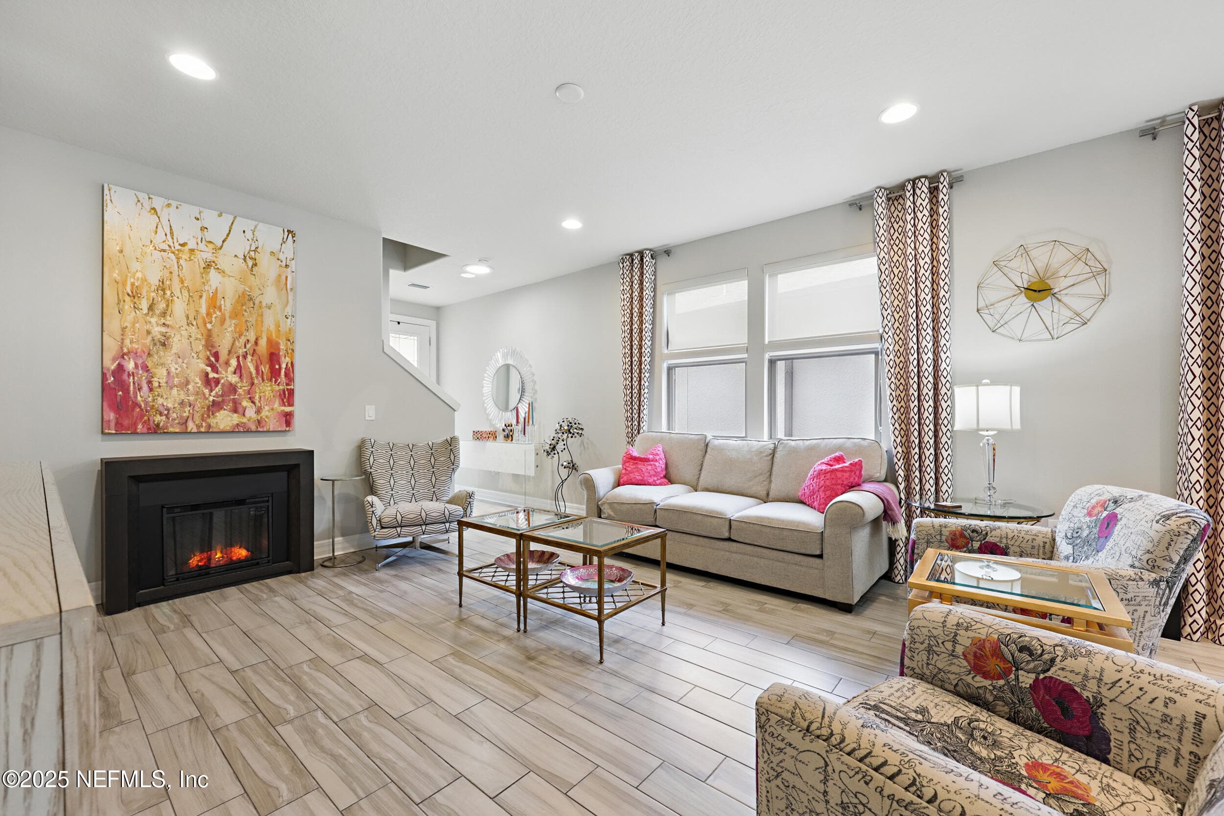 Living room (fireplace wall) — Living room featuring an electric fireplace with dark surround, large windows with natural light, wood-look tile flooring, recessed lighting, and open sightline to the foyer and staircase. — 92 CANOPY OAK Lane, Ponte Vedra, FL 32081