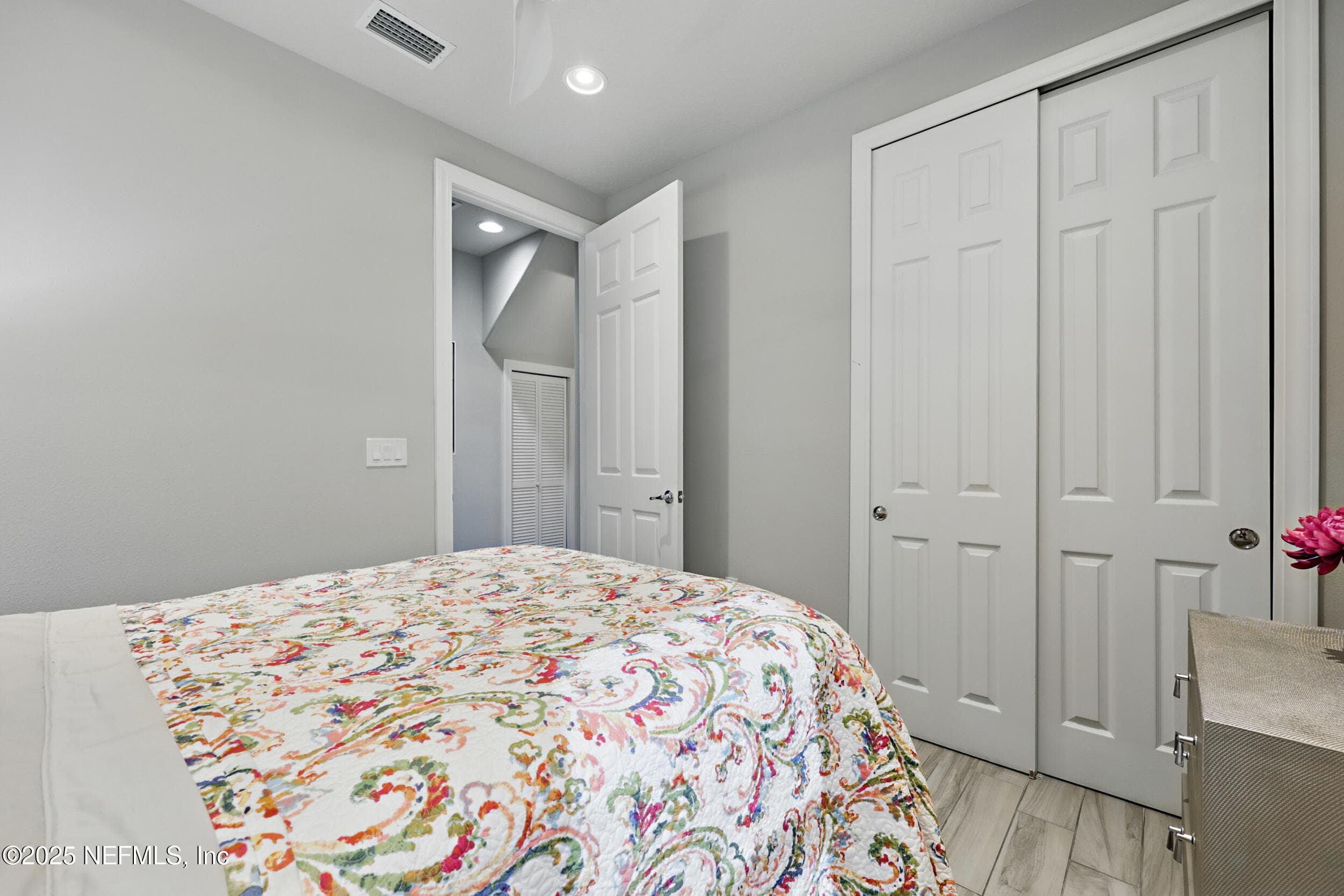 Second bedroom (closet wall) — Guest bedroom with double-door closet, recessed lighting, wood-look tile flooring, and hallway access to a shared bathroom. Utility closet with louvered doors visible in the hall. — 92 CANOPY OAK Lane, Ponte Vedra, FL 32081