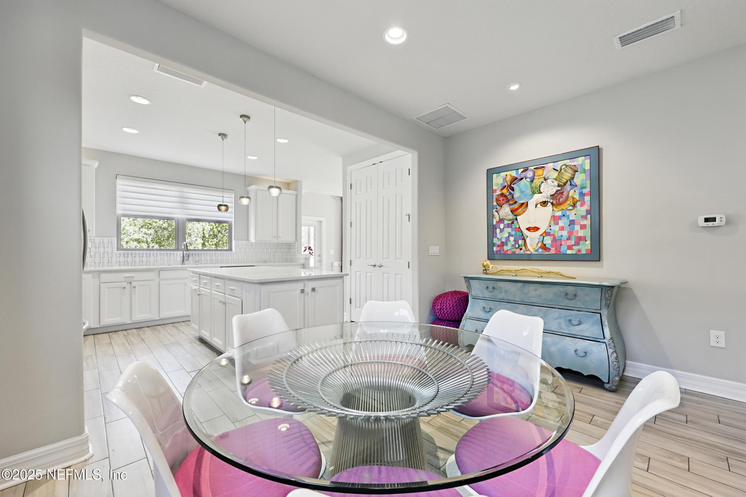 Dining area toward kitchen — View from the dining area into the kitchen showing white shaker cabinetry, white countertop island, pendant lights, tile backsplash, pantry closet, and wood-look tile flooring. — 92 CANOPY OAK Lane, Ponte Vedra, FL 32081