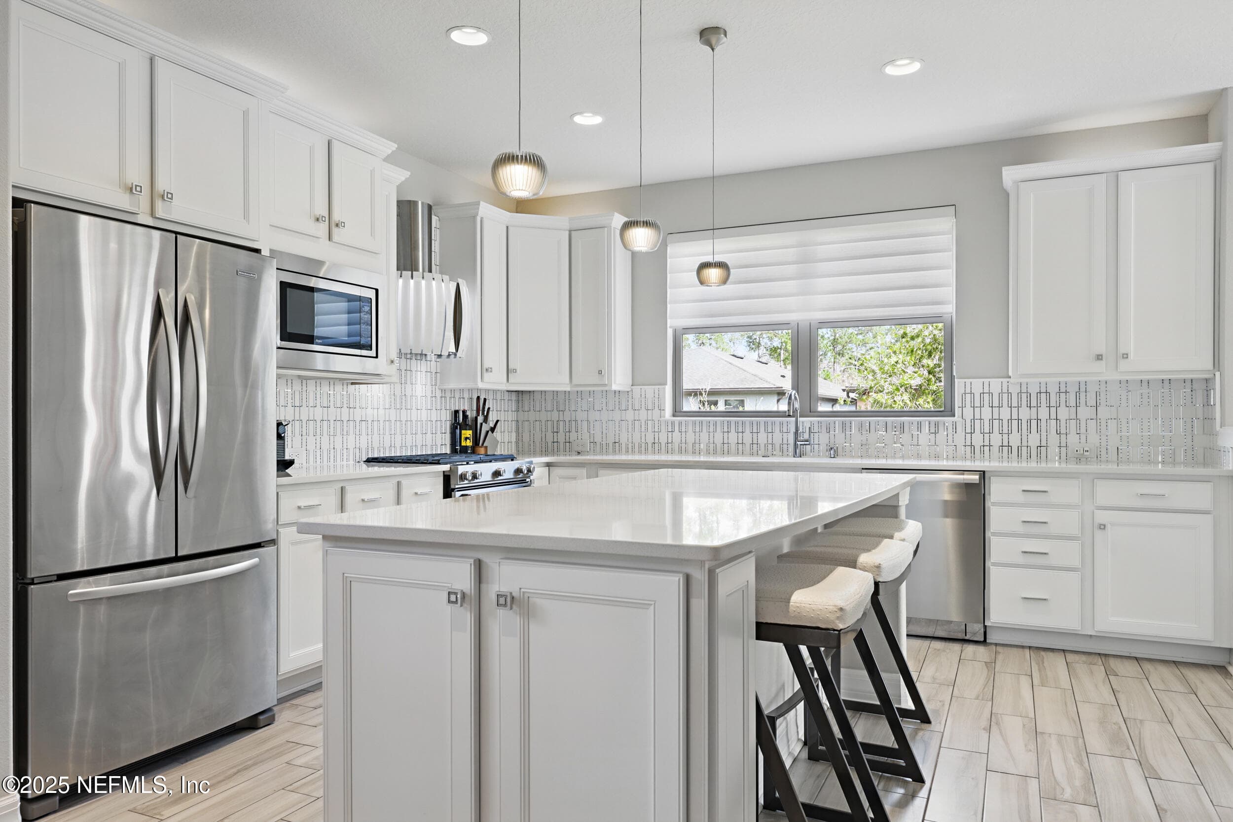 Kitchen — Kitchen with white quartz countertops, white shaker cabinetry, gas range, custom vent hood, stainless steel French door refrigerator, built-in microwave, geometric tile backsplash, pendant lighting over the center island with barstool seating, and wood-look tile flooring. — 92 CANOPY OAK Lane, Ponte Vedra, FL 32081