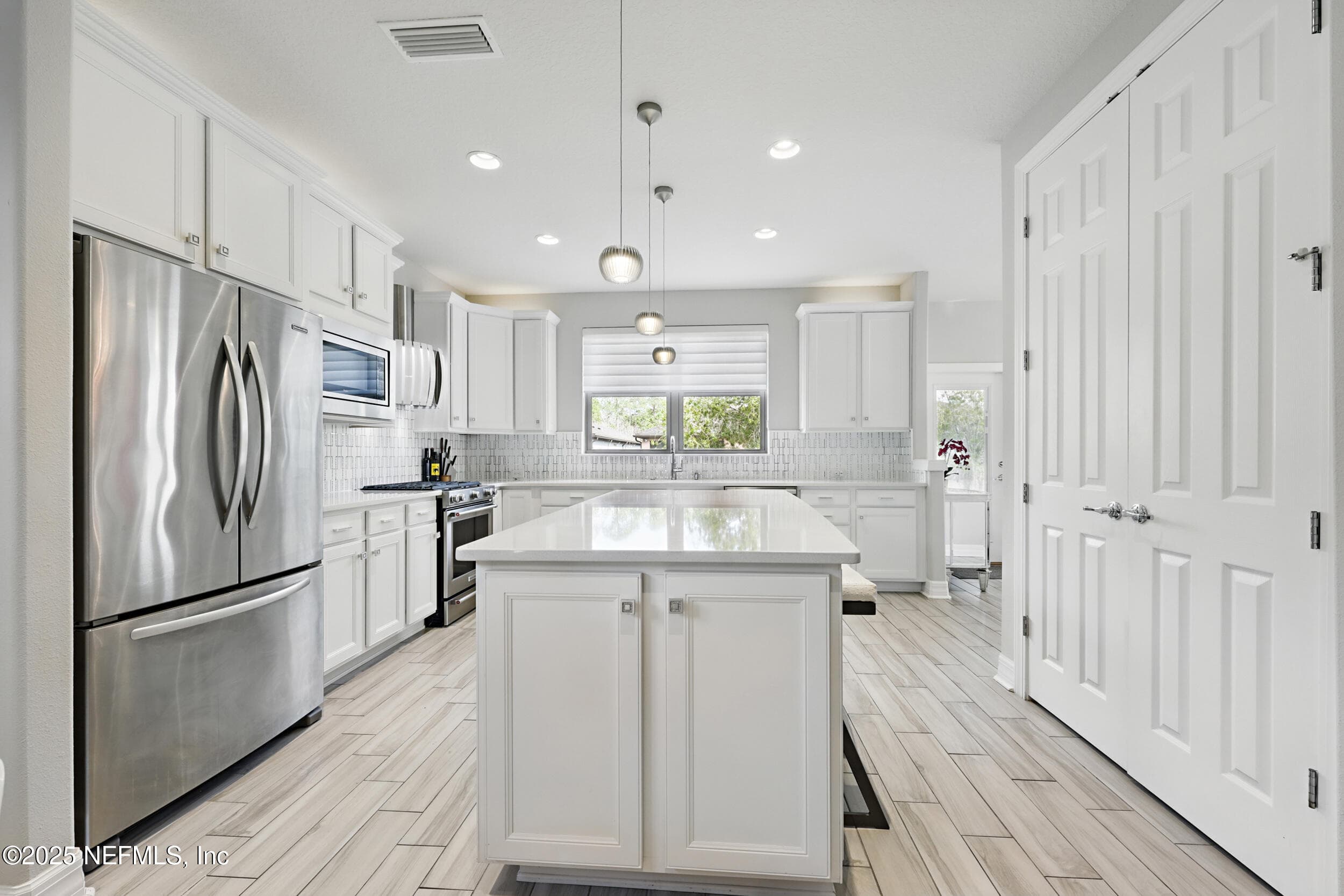 Kitchen (alternate angle) — Kitchen with white quartz countertops, white shaker cabinetry with crown molding, center island with cabinet storage, stainless steel French door refrigerator, gas range, custom vent hood, geometric tile backsplash, pendant lighting, and pantry closet with double doors. — 92 CANOPY OAK Lane, Ponte Vedra, FL 32081