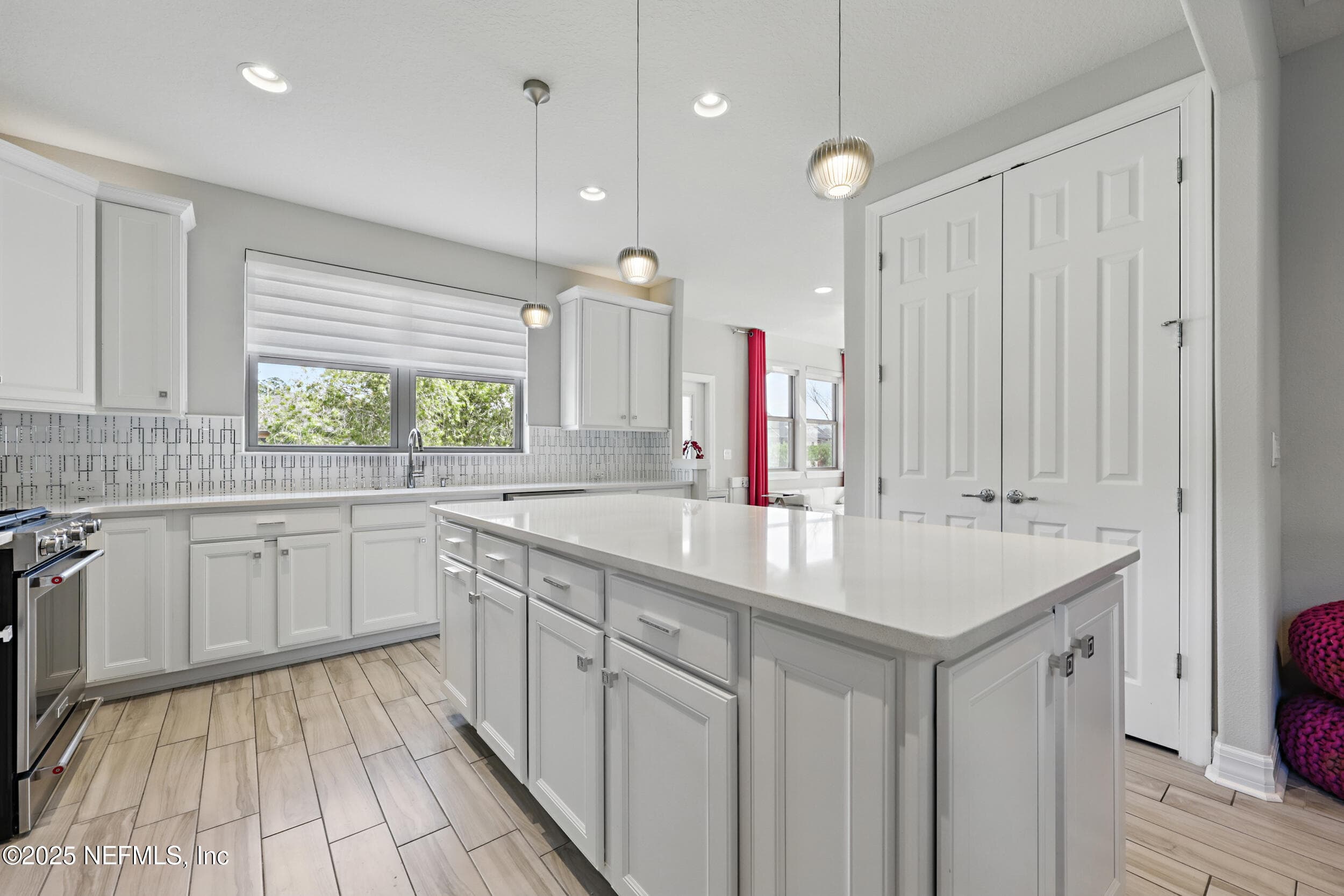 Kitchen (island detail) — Center island with white quartz countertop, shaker cabinet storage, and pendant lighting above. Geometric tile backsplash extends wall to wall with window above the sink area. Double-door pantry closet adjacent to the kitchen. — 92 CANOPY OAK Lane, Ponte Vedra, FL 32081