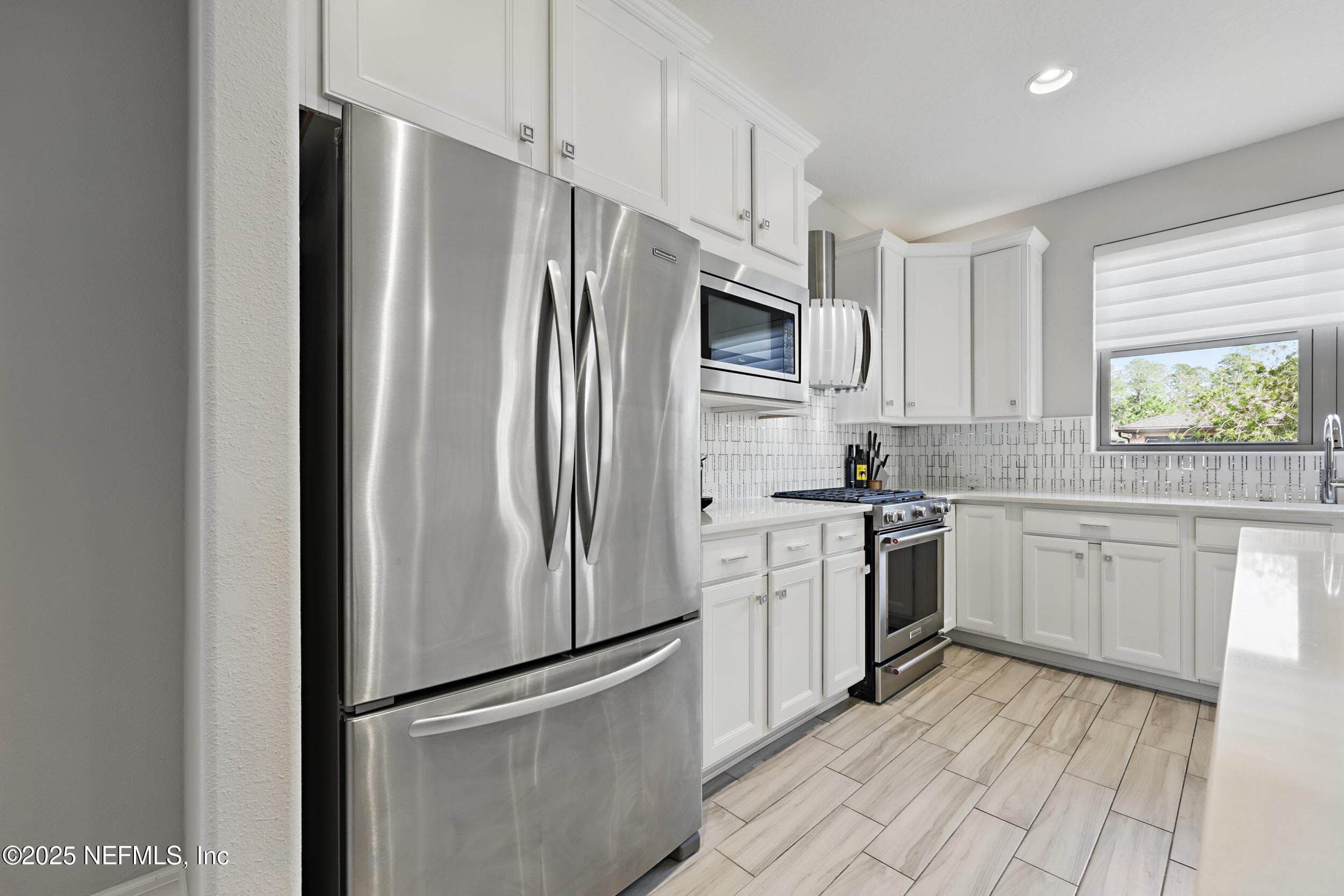 Kitchen (refrigerator wall) — Stainless steel French door refrigerator, built-in microwave, custom vent hood, gas range, geometric tile backsplash, white shaker cabinetry with square nickel hardware, and wood-look tile flooring. — 92 CANOPY OAK Lane, Ponte Vedra, FL 32081