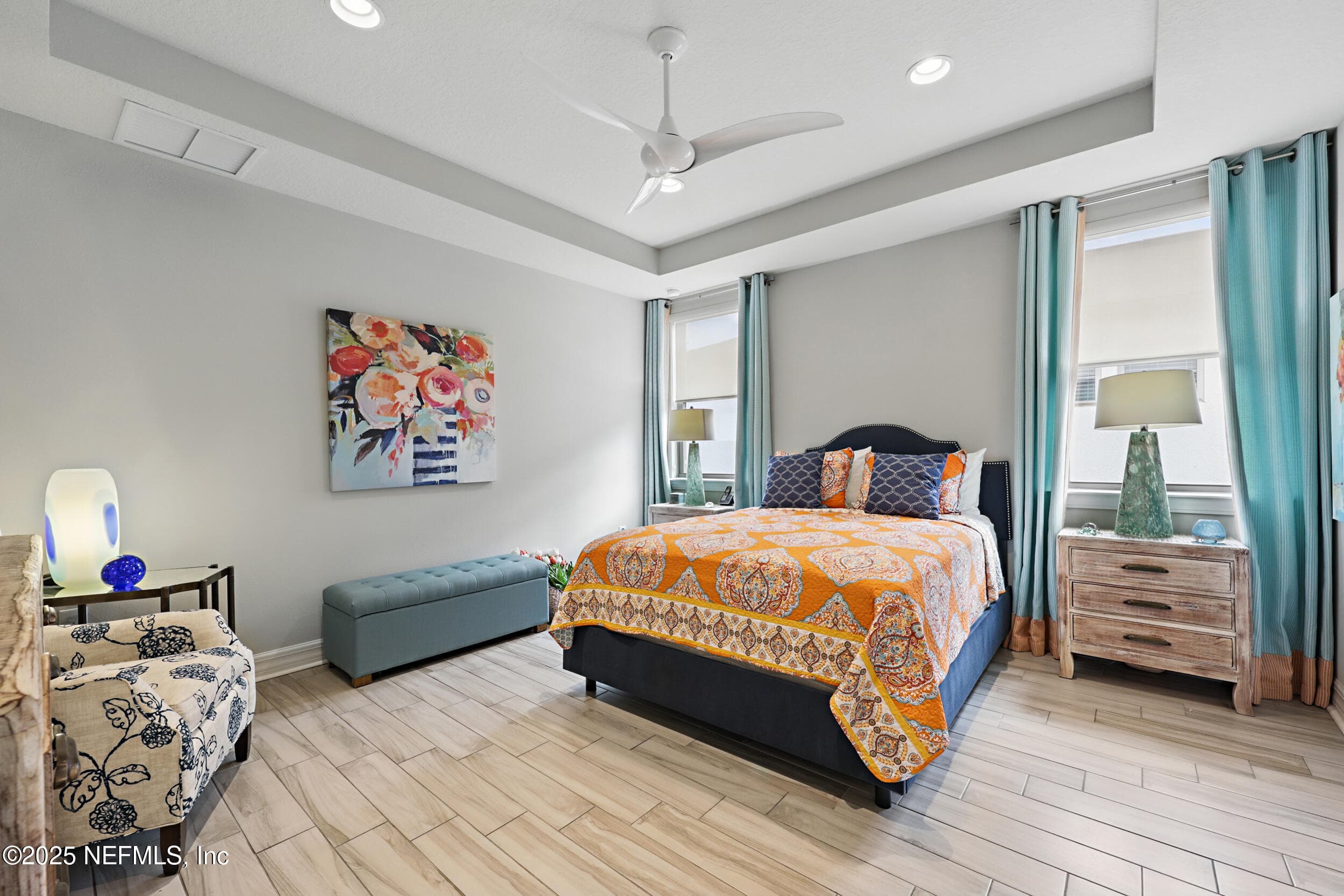 Primary bedroom — First-floor primary bedroom with tray ceiling, modern three-blade ceiling fan, recessed lighting, wood-look tile flooring, multiple windows with custom curtain panels and roller shades, and room for a seating area. — 92 CANOPY OAK Lane, Ponte Vedra, FL 32081