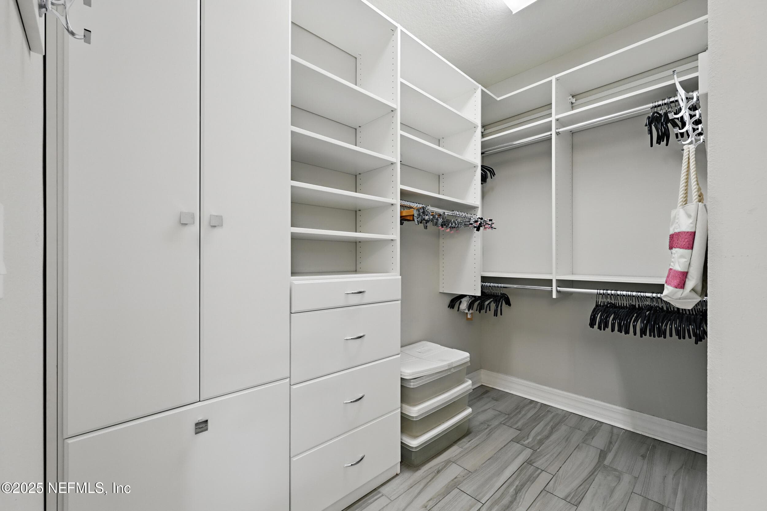Primary walk-in closet — Primary walk-in closet with custom built-in organizer system featuring adjustable shelving, drawers, and double hanging rods. Wood-look tile flooring and overhead lighting. — 92 CANOPY OAK Lane, Ponte Vedra, FL 32081