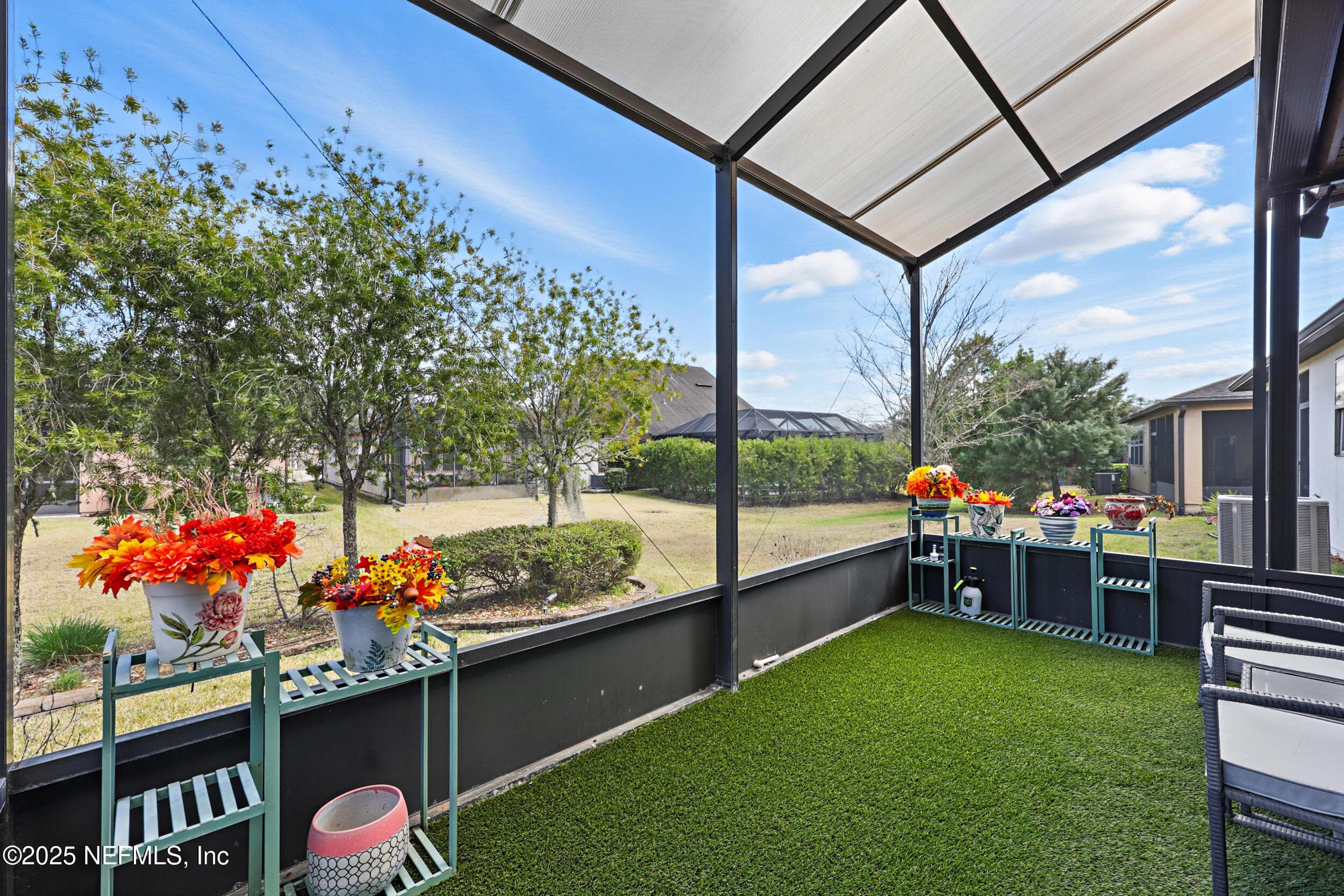 Screened lanai (yard view) — Screened-in lanai with artificial turf flooring, covered roof, and open view of the backyard with mature trees and landscaped hedges. Accessible from the first-floor sitting room. — 92 CANOPY OAK Lane, Ponte Vedra, FL 32081