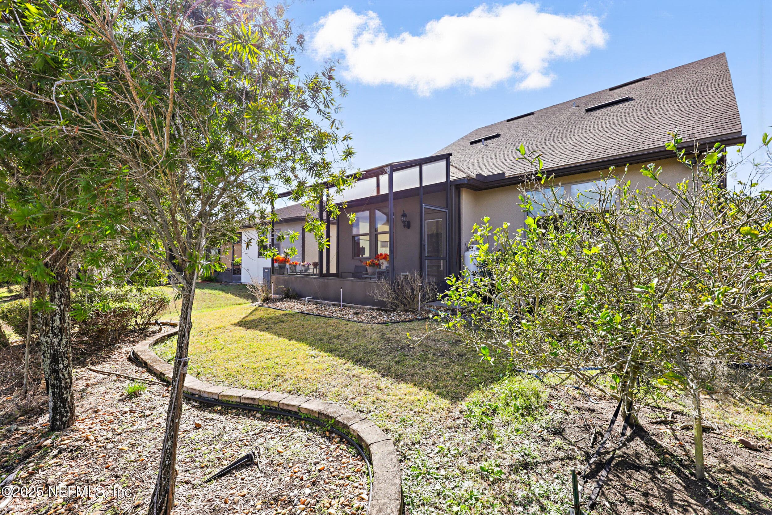 Rear exterior — Rear view of the two-story stucco home with screened lanai, architectural shingle roof, paver-edged landscape beds with mature trees, shrubs, and drip irrigation system throughout the backyard. — 92 CANOPY OAK Lane, Ponte Vedra, FL 32081