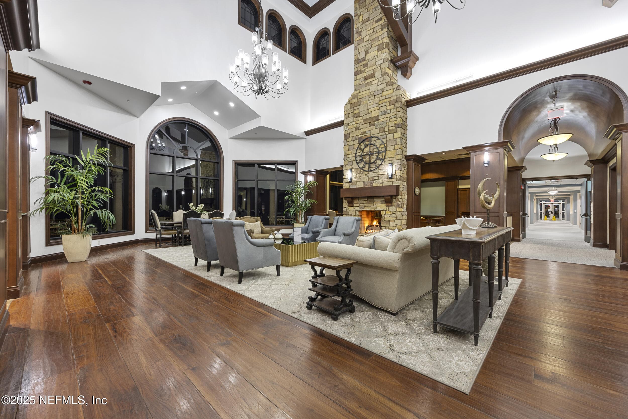 Anastasia Clubhouse lobby (fireplace lounge) — Clubhouse lobby lounge with floor-to-ceiling stacked stone fireplace, hardwood flooring, crystal chandeliers, arched windows, and arched corridor leading to the ballroom, café, and activity rooms within the Anastasia Clubhouse. — 92 CANOPY OAK Lane, Ponte Vedra, FL 32081