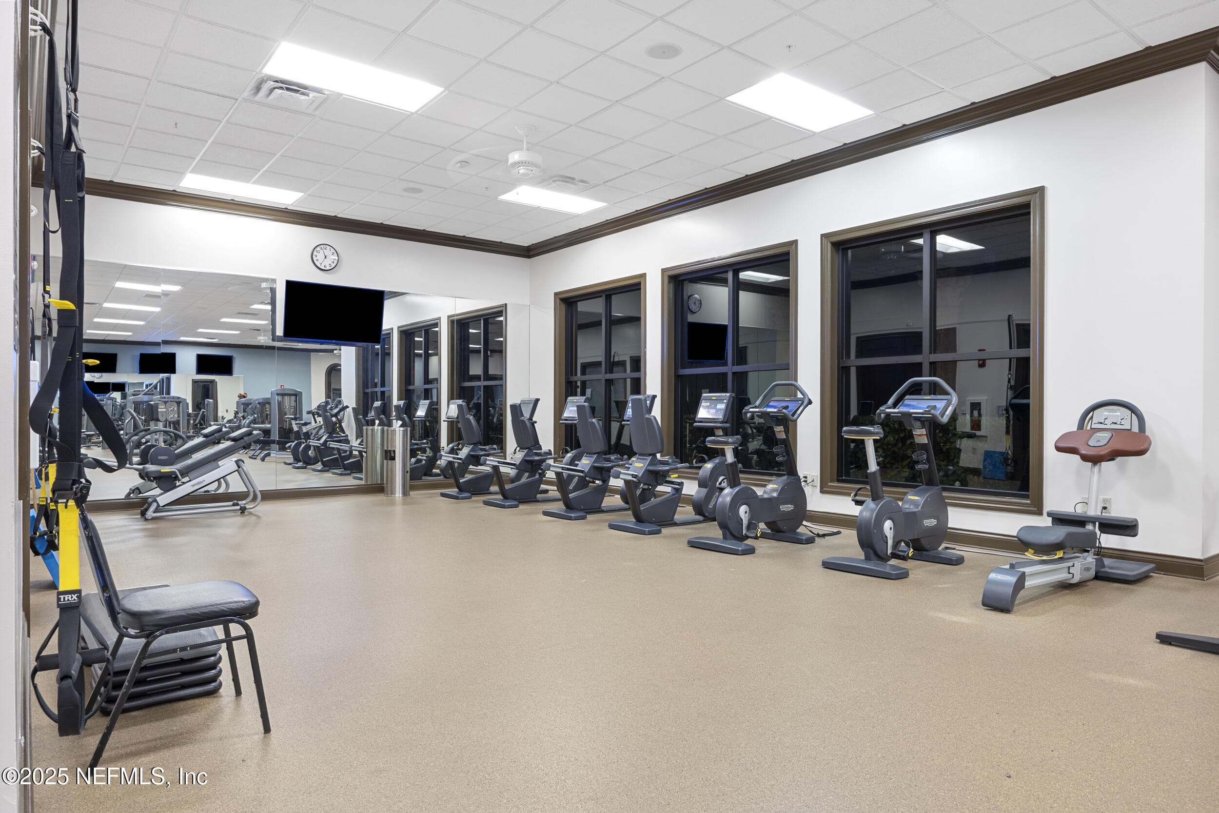 Anastasia Clubhouse fitness center (cycling and rowing) — Fitness center with stationary cycling bikes, rowing machines, TRX suspension station, wall-mounted TV, mirrored walls, and windows overlooking the clubhouse grounds inside the Anastasia Clubhouse. — 92 CANOPY OAK Lane, Ponte Vedra, FL 32081