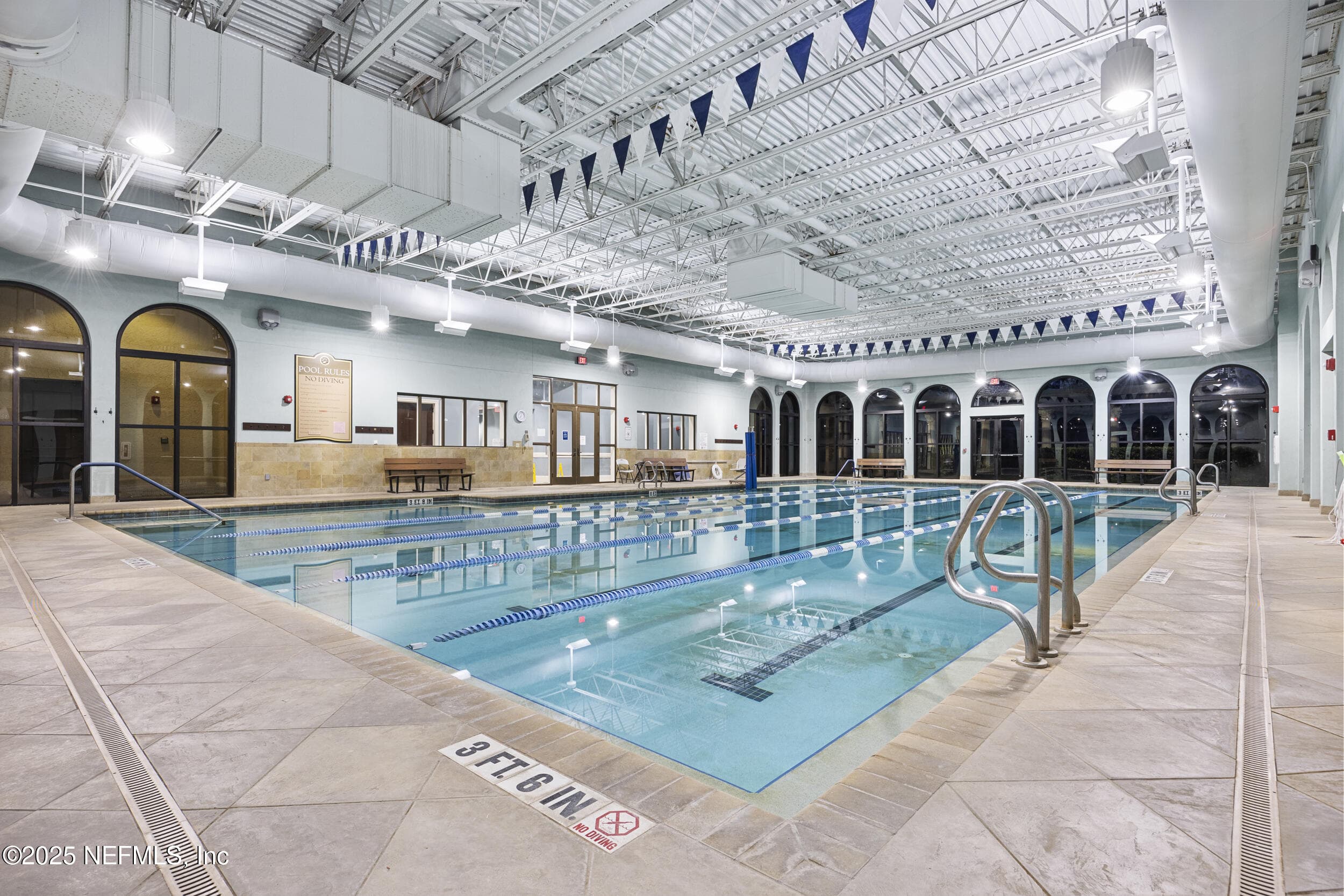 Anastasia Clubhouse indoor lap pool — Indoor heated lap pool with marked swim lanes, tile deck, arched windows, high open-truss ceiling, and handrail entry inside the 37,000 sq ft Anastasia Clubhouse at Del Webb Ponte Vedra. — 92 CANOPY OAK Lane, Ponte Vedra, FL 32081
