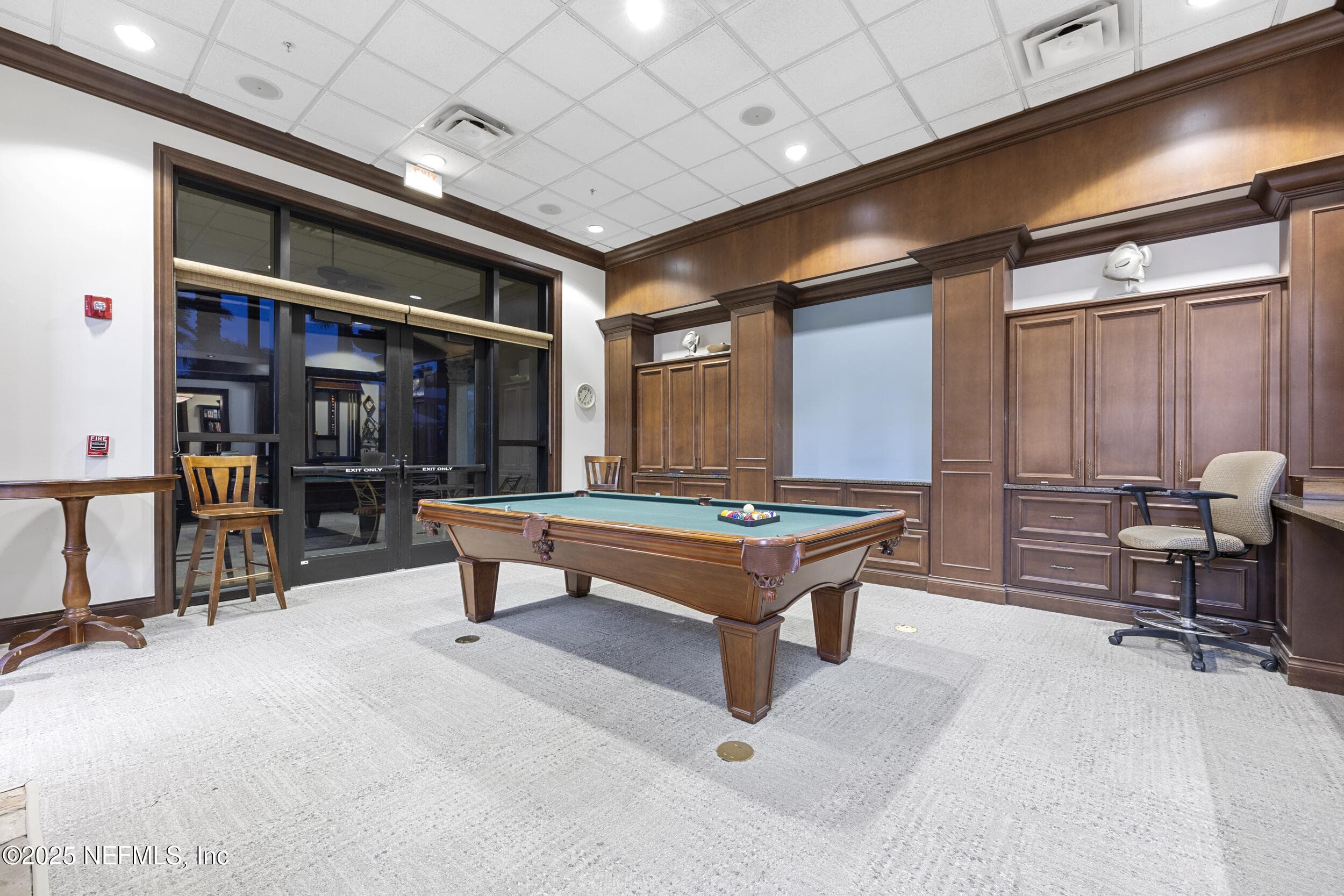 Anastasia Clubhouse billiards room — Billiards and pool room inside the Anastasia Clubhouse with full-size pool table, dark wood built-in cabinetry, barstool seating, and glass doors opening to the main corridor at Del Webb Ponte Vedra. — 92 CANOPY OAK Lane, Ponte Vedra, FL 32081