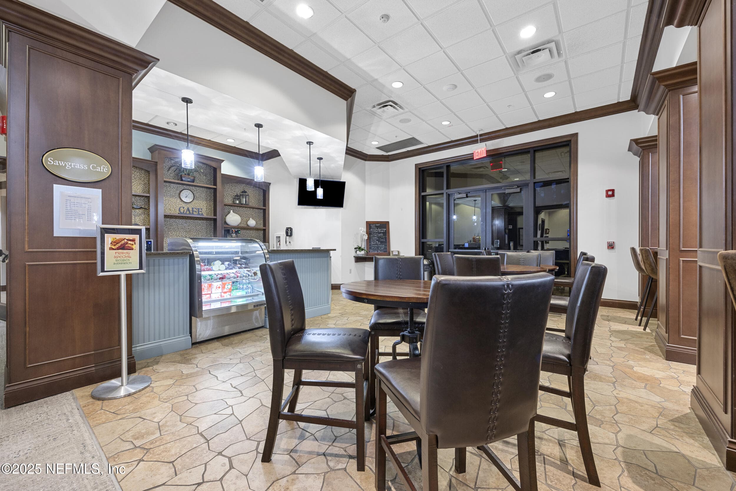 Anastasia Clubhouse Sawgrass Café — Sawgrass Café inside the Anastasia Clubhouse with counter service, display case, pendant lighting, pub-height tables and chairs, wall-mounted TV, and stone tile flooring. On-site dining for Del Webb Ponte Vedra residents. — 92 CANOPY OAK Lane, Ponte Vedra, FL 32081