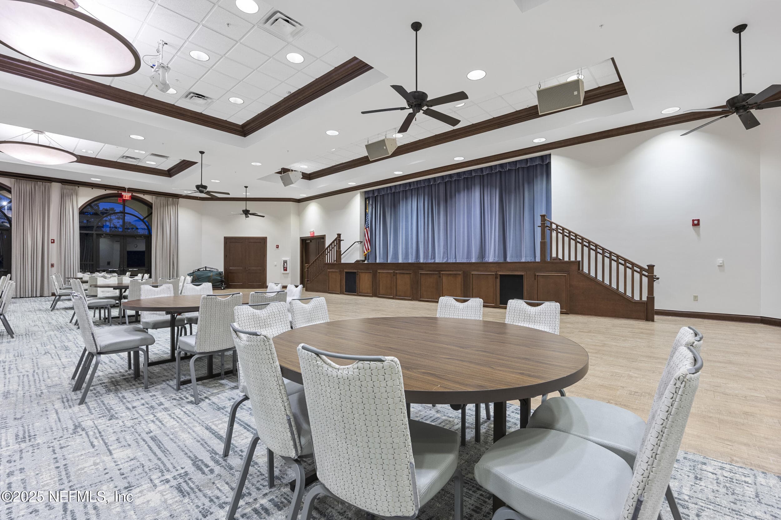 Anastasia Clubhouse ballroom (stage view) — Ballroom with elevated performance stage, curtain backdrop, dance floor, round banquet tables, tray ceiling with oversized light fixtures, and ceiling fans inside the Anastasia Clubhouse. — 92 CANOPY OAK Lane, Ponte Vedra, FL 32081