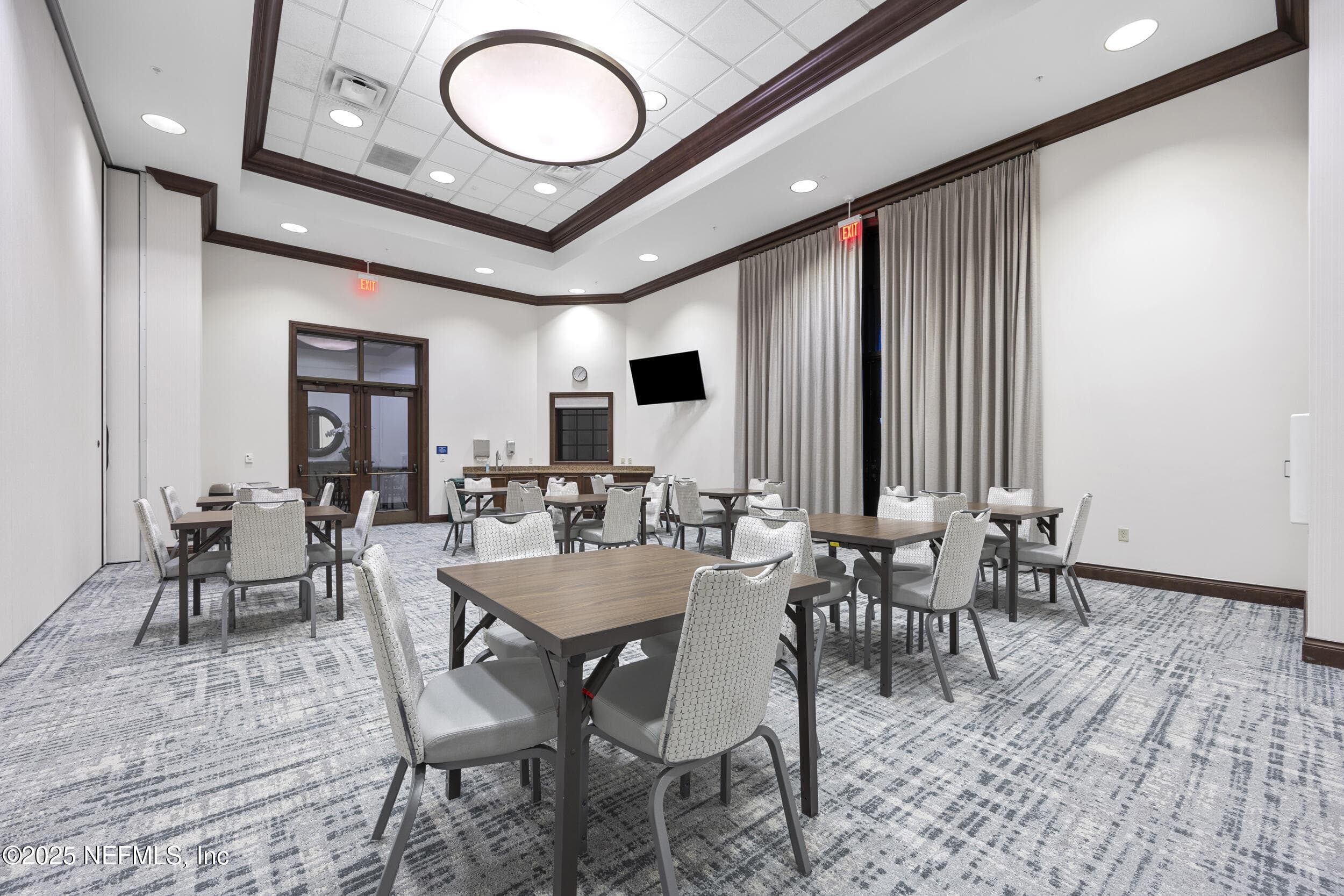 Anastasia Clubhouse meeting room — Private meeting and event room inside the Anastasia Clubhouse with banquet seating, tray ceiling with oversized circular light fixture, wall-mounted TV, wet bar, and room-divider curtain for flexible use at Del Webb Ponte Vedra. — 92 CANOPY OAK Lane, Ponte Vedra, FL 32081