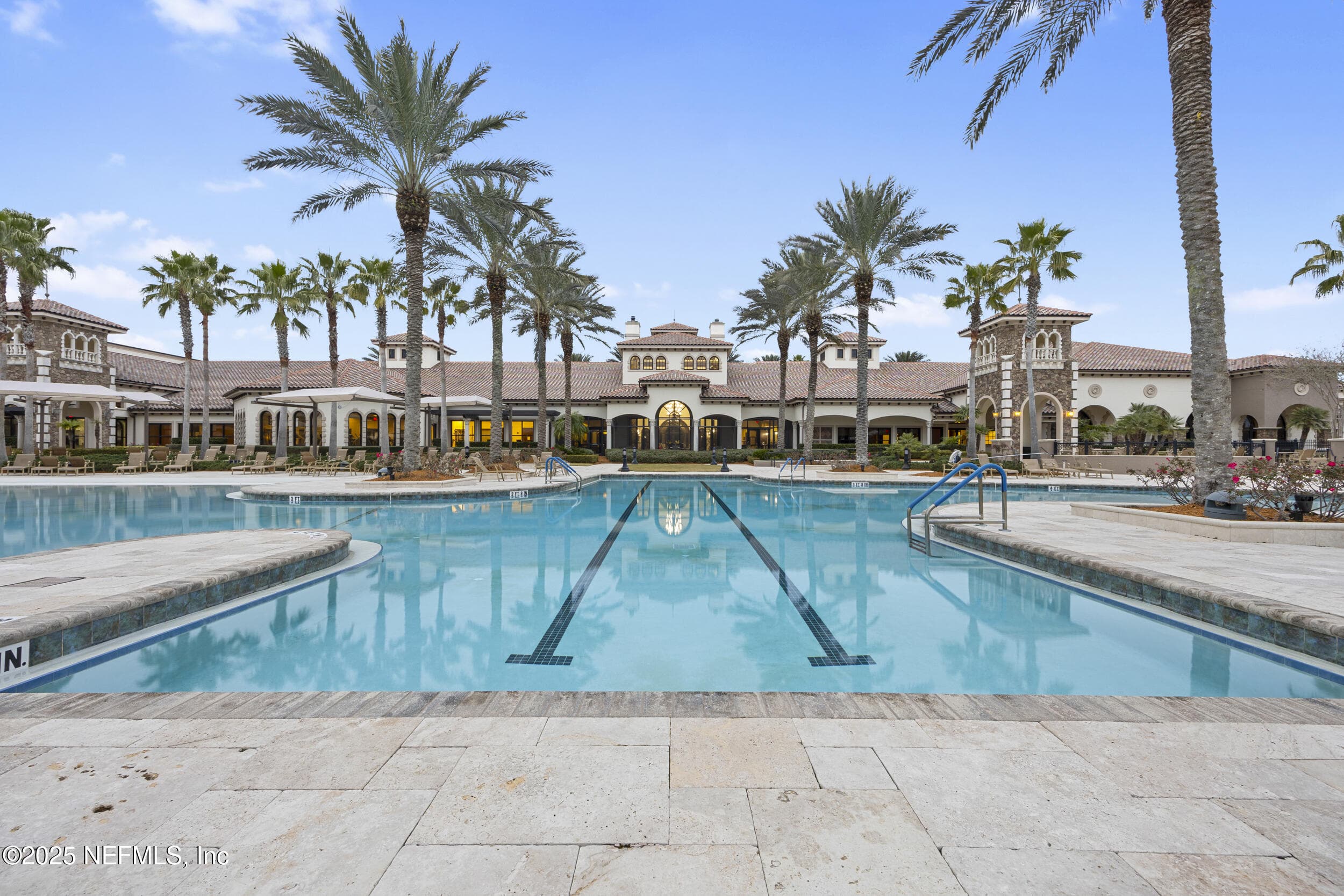 Del Webb Ponte Vedra outdoor pool and clubhouse — Outdoor pool with lap lanes and beach entry looking back toward the Anastasia Clubhouse Mediterranean-style façade with arched colonnades, clay tile roof, and palm tree landscaping at Del Webb Ponte Vedra. — 92 CANOPY OAK Lane, Ponte Vedra, FL 32081