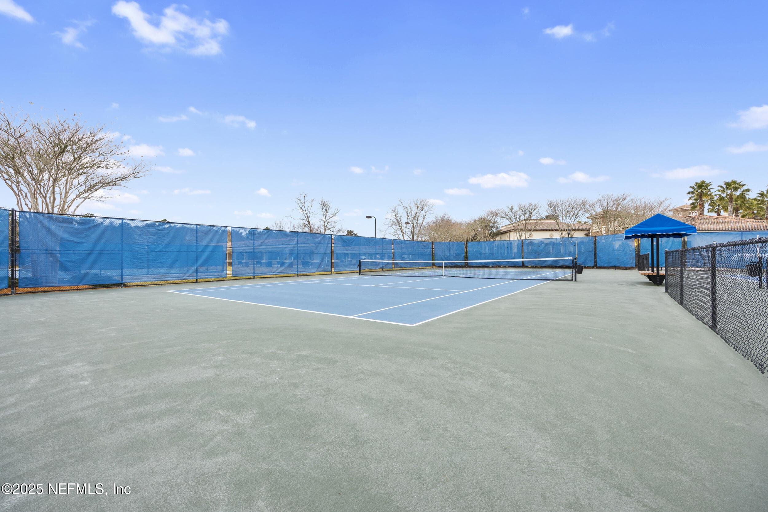 Del Webb Ponte Vedra pickleball court — Hard-surface pickleball court with blue playing surface, windscreens, perimeter fencing, night lighting, and shaded spectator area at Del Webb Ponte Vedra. — 92 CANOPY OAK Lane, Ponte Vedra, FL 32081