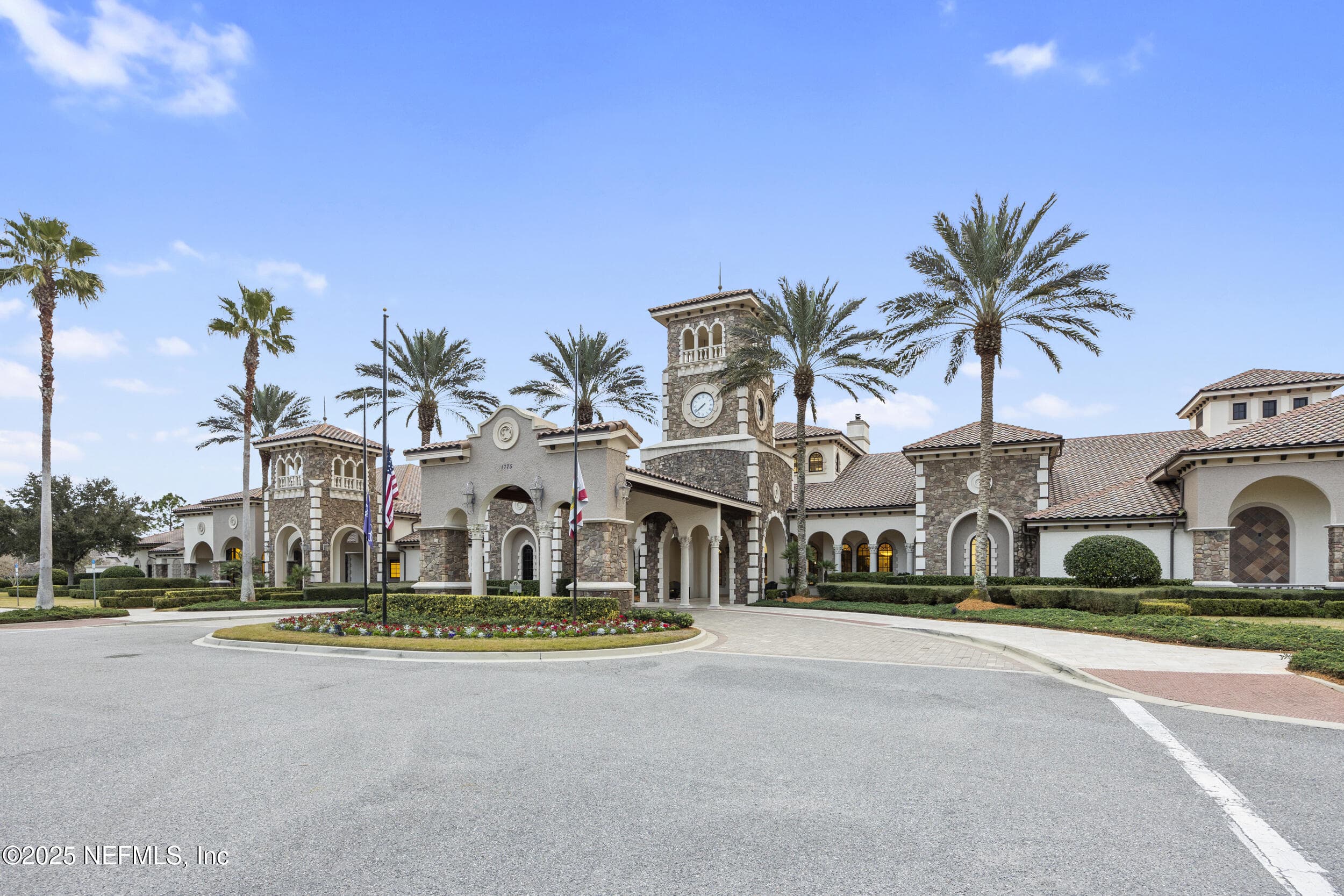 Anastasia Clubhouse exterior — Del Webb Ponte Vedra's 37,000-square-foot Anastasia Clubhouse with Mediterranean-style stone and stucco architecture, clock tower, clay tile roof, arched entryways, porte-cochère, manicured landscaping, and palm-lined circular drive. — 92 CANOPY OAK Lane, Ponte Vedra, FL 32081