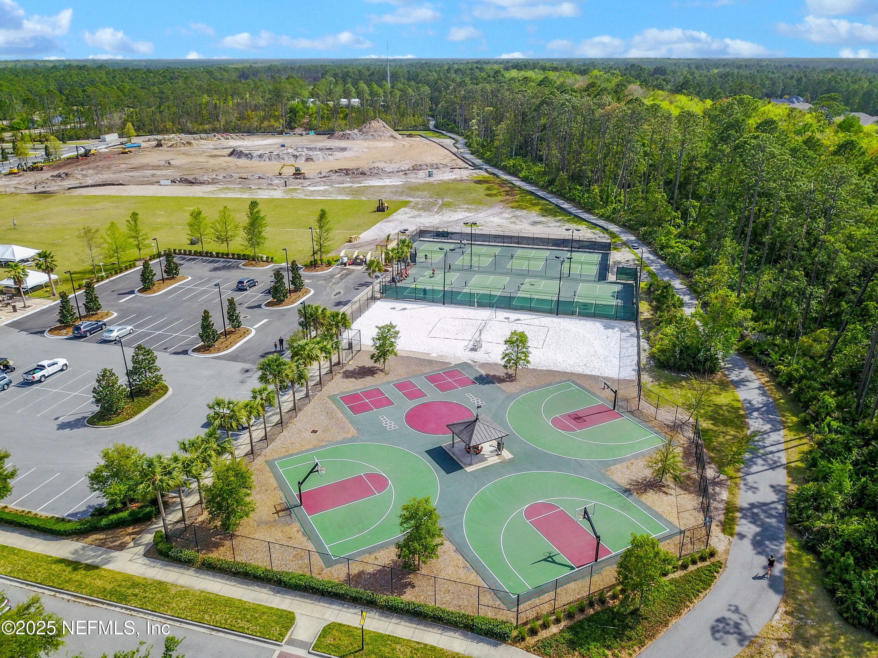 Nocatee sports complex (aerial) — Aerial view of the Nocatee sports complex featuring multiple basketball courts, pickleball courts, sand volleyball courts, lighted playing fields, covered pavilion, and palm-lined parking area surrounded by preserve. — 92 CANOPY OAK Lane, Ponte Vedra, FL 32081
