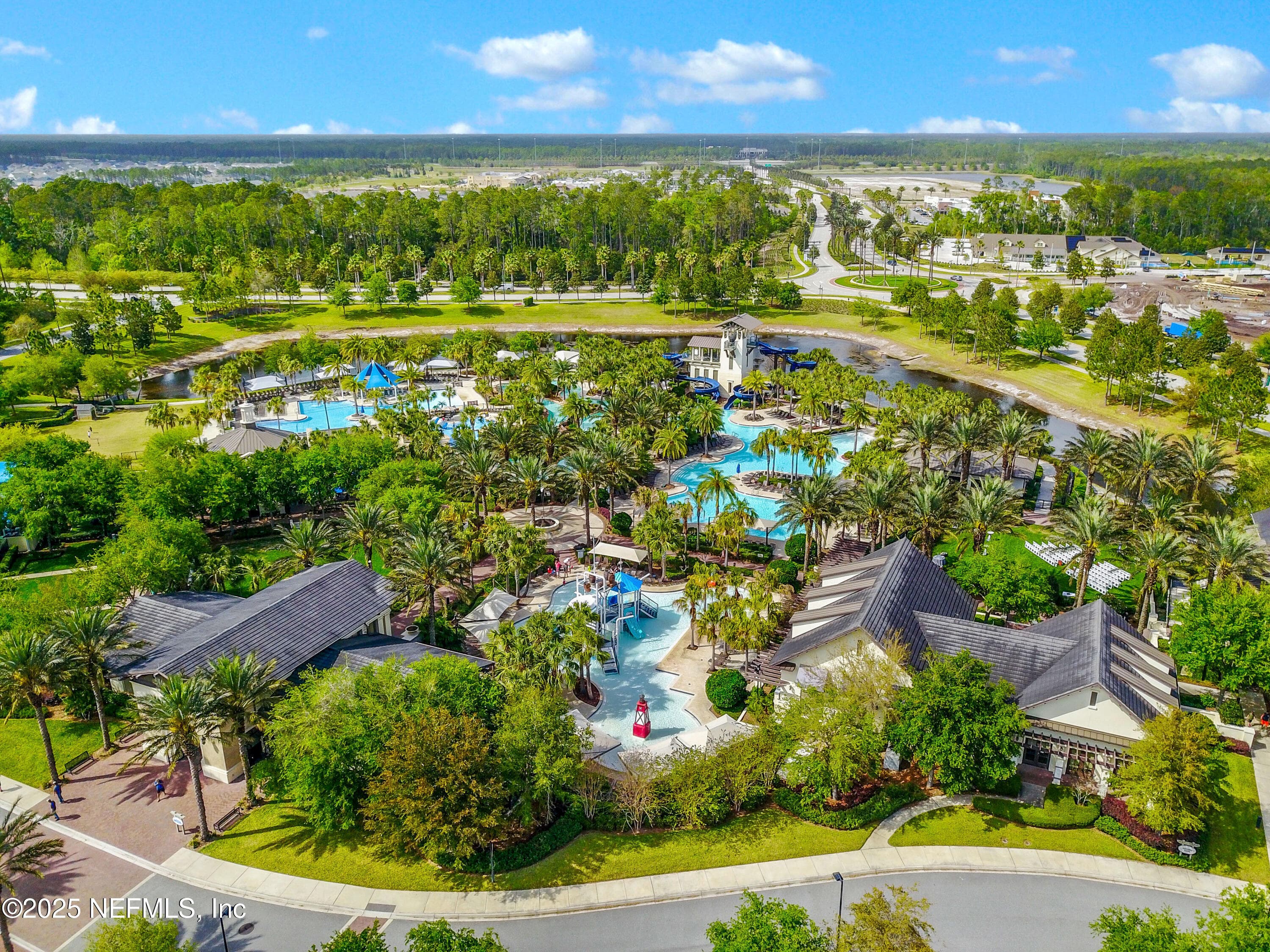 Nocatee Splash Water Park (aerial wide) — Aerial view of the Nocatee Splash Water Park featuring resort-style pools, high-speed waterslides from the tower, splash pads, lazy river, palm tree landscaping, pavilions, and pond-side setting. — 92 CANOPY OAK Lane, Ponte Vedra, FL 32081