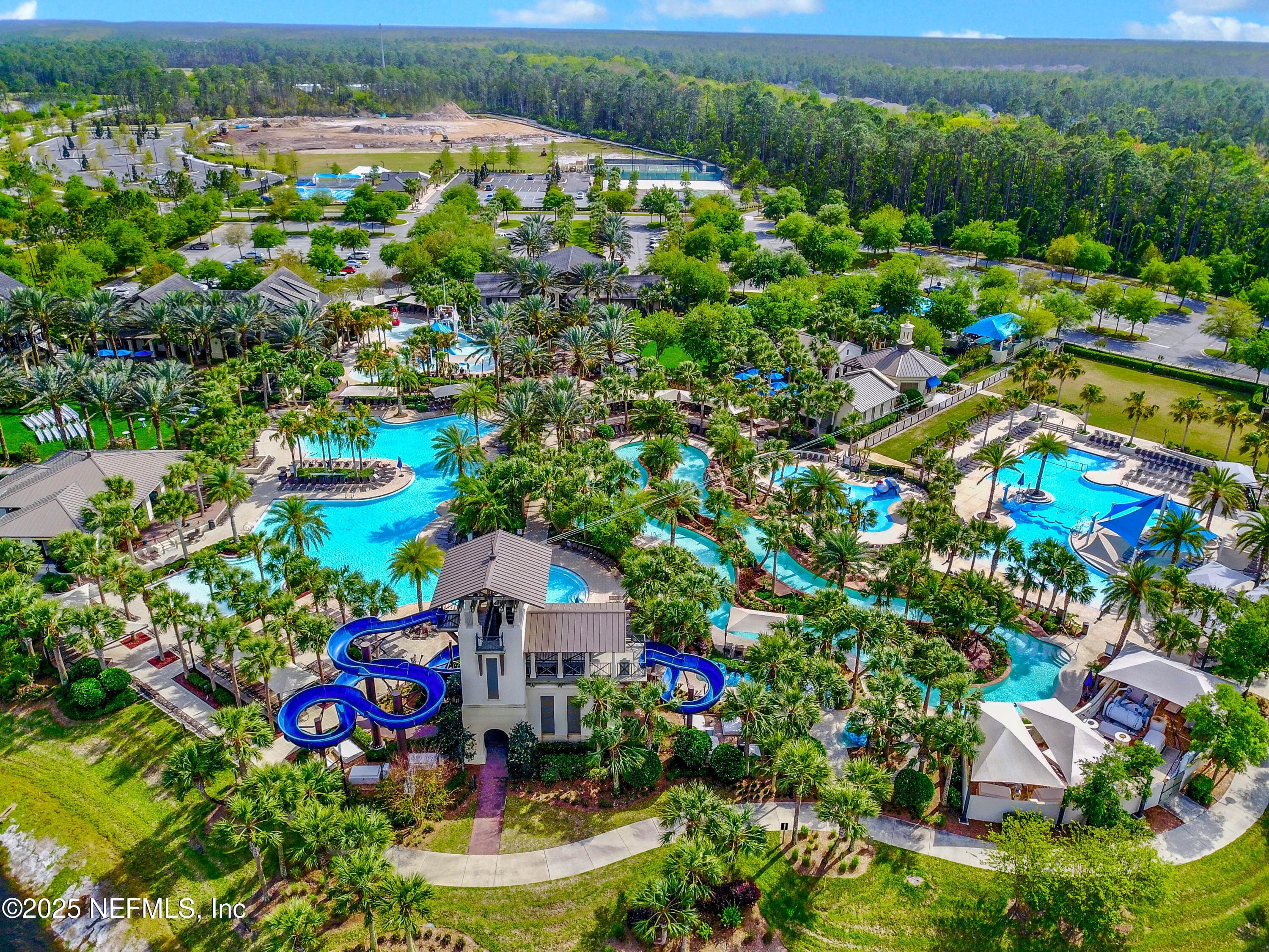 Nocatee Splash Water Park (aerial close) — Aerial view of the Nocatee Splash Water Park showing dual high-speed waterslides, multiple resort-style pools, lazy river, splash areas, cabanas, covered pavilions, and lush tropical landscaping throughout the park. — 92 CANOPY OAK Lane, Ponte Vedra, FL 32081