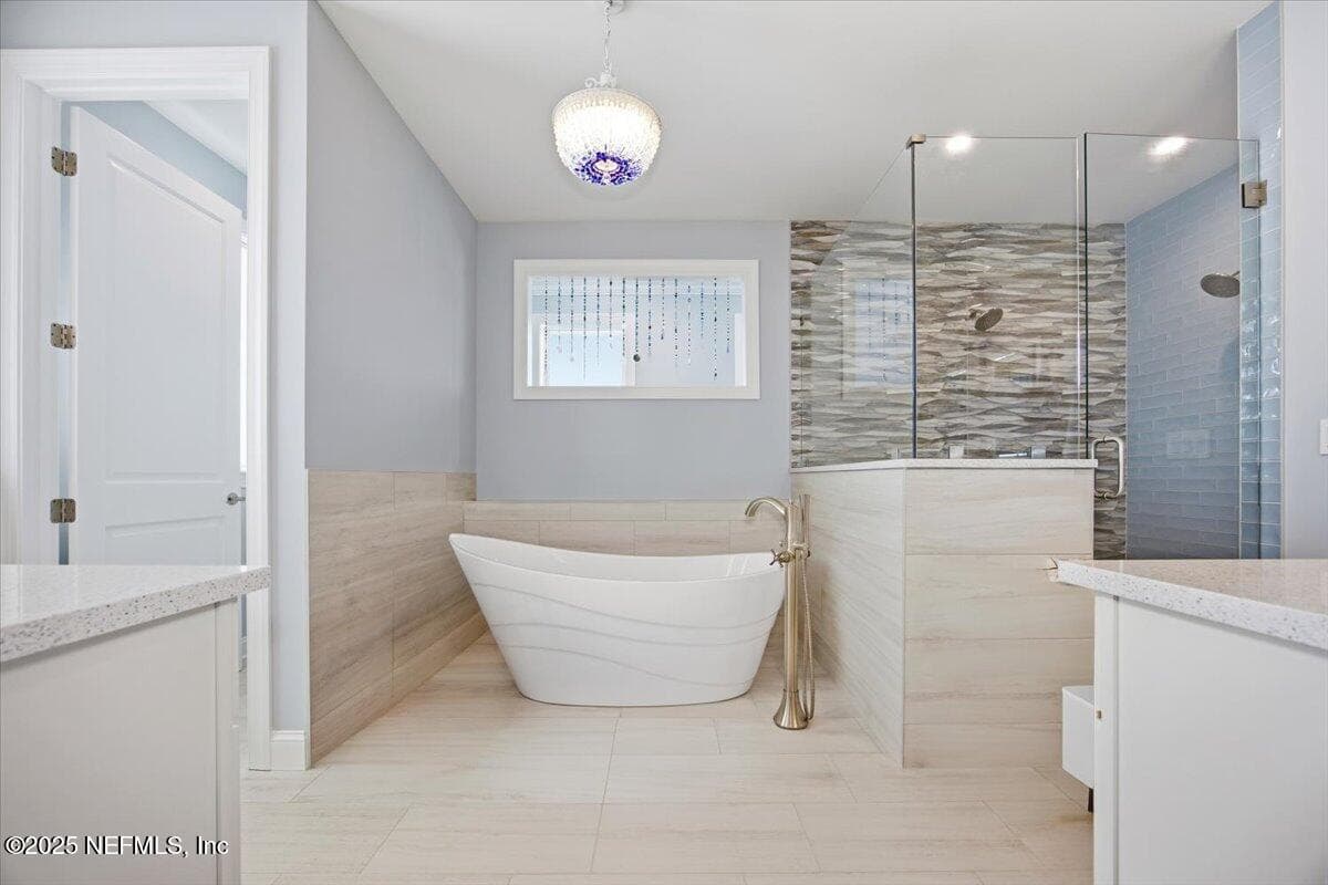 Soaker tub and HUGE shower with 3 shower heads. Tile was all chosen to have the "beach" feel. The light is sea glass, and the beads in the open area were made by a designer friend. It opens to the back stairwell to let light in. — 4 SUMMER Court, Jacksonville Beach, FL 32250