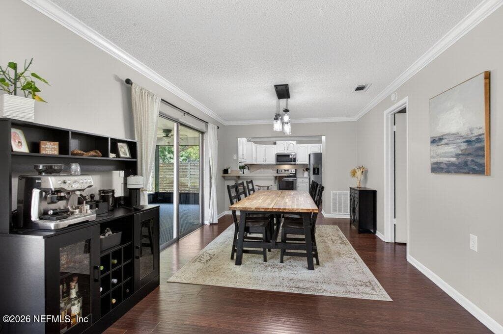 An open-concept dining area that flows seamlessly into the kitchen, characterized by laminate flooring, crisp crown molding, and large sliding glass doors that invite ample natural light. — 956 ESPINADO Avenue, St. Augustine, FL 32086