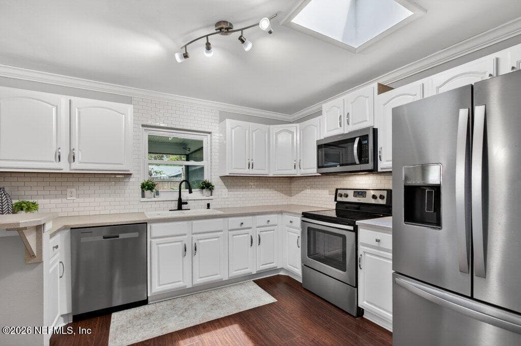 A bright, renovated kitchen featuring a skylight, recessed track lighting, a classic subway tile backsplash, and sleek stainless steel appliances. — 956 ESPINADO Avenue, St. Augustine, FL 32086